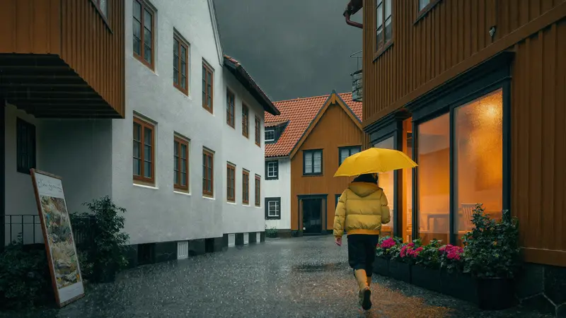 Person with a yellow umbrella on a rainy cobblestone street in Bergen old town