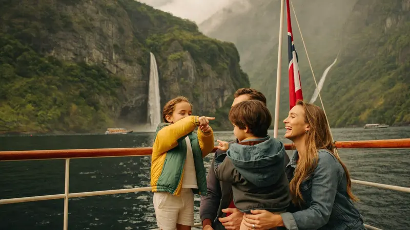 Family with young children pointing at a waterfall from a fjord sightseeing boat
