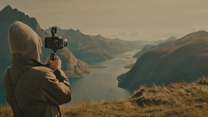 Travel filmmaker recording a fjord panorama from a clifftop