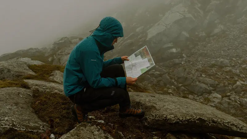 Hiker in rain gear checking a map on a foggy Norwegian mountain trail