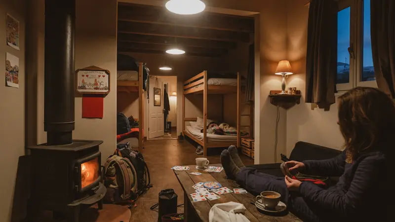 Cosy budget mountain hostel common room with travelers by a wood stove