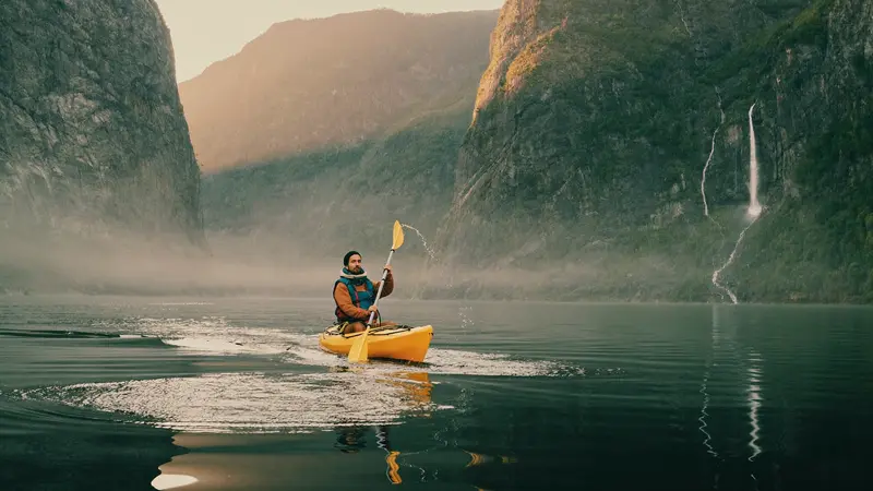 Sea kayaker gliding across a mirror-still fjord at dawn