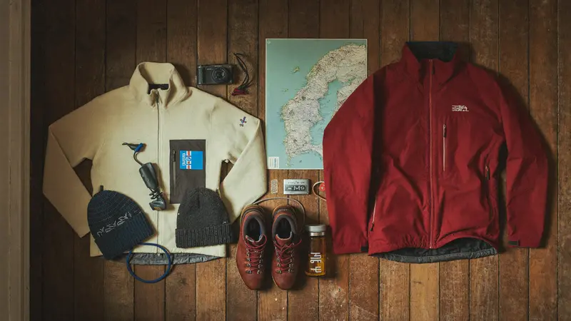 Flat lay of Norway packing essentials: wool layers, shell jacket, boots and a fjord map