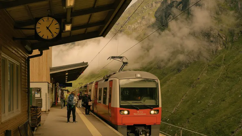 Red regional train at a small Norwegian mountain station with hikers boarding