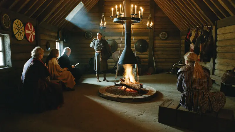 Costumed Viking reenactor by a fire in a timber longhouse at Gudvangen